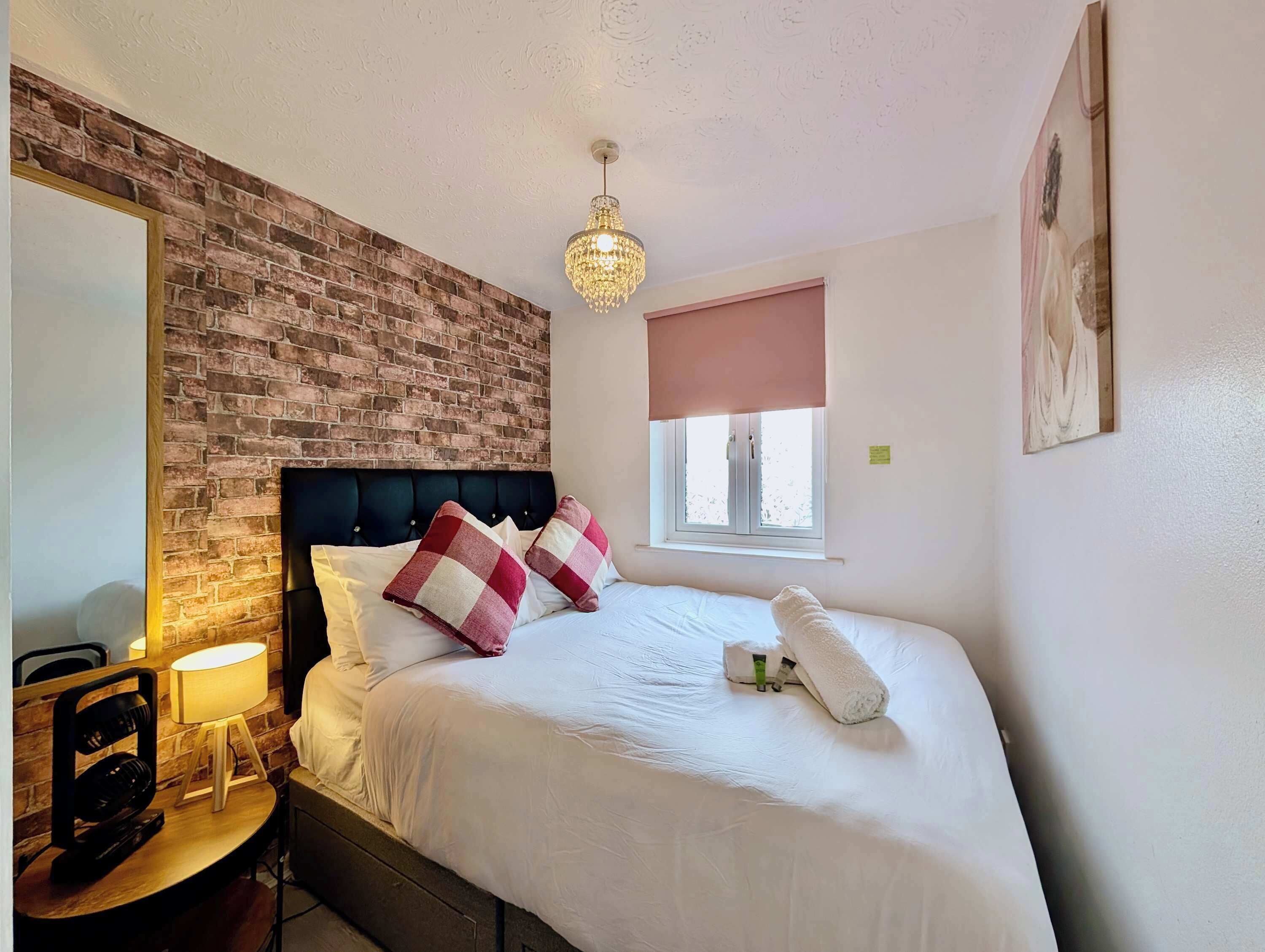 A hotel room with a brick accent wall, a bed with white bedding and checkered pillows, a bedside lamp, and a window with a view.