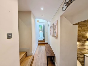 A hallway with a wooden bench, a staircase, and a brick wall. - Stunning 2Bed flat with private patio (Greater London)