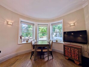 Ein Essbereich mit Tisch und Stühlen, drei Fenstern mit Aussicht, einem Flachbildfernseher und einer Holzkommode.