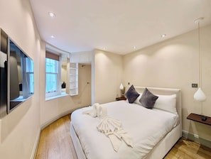 A modern bedroom with a large bed, a built-in wardrobe, a bedside table, and a mirror. - Stunning 2Bed flat with private patio (Greater London)
