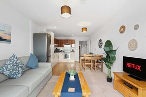 A modern living room with a sofa, coffee table, and a TV. There is a kitchen in the background with cabinets and a dining area. - Stunning Two-Level Apartment in Brighton (Brighton and Hove)
