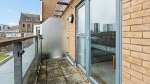 A balcony with a glass door, a metal railing, and a view of a building in the background. - Stunning Two-Level Apartment in Brighton (Brighton and Hove)