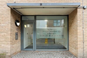 Entrada de um edifício com porta de vidro, alarme de incêndio e placa indicando The Barrows Apartments na Francis Street, com números de contato.