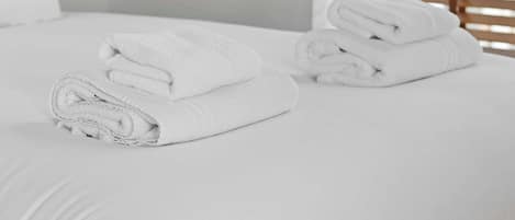 A hotel room with a bed, a window with blinds, and a folded towel on the bed.
