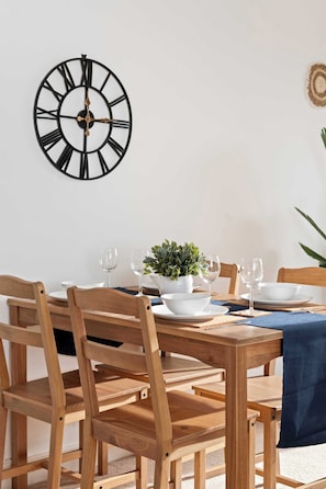 A dining area with a wooden table set for four, a wall-mounted clock, and a potted plant. - Stunning Two-Level Apartment in Brighton (Brighton and Hove)