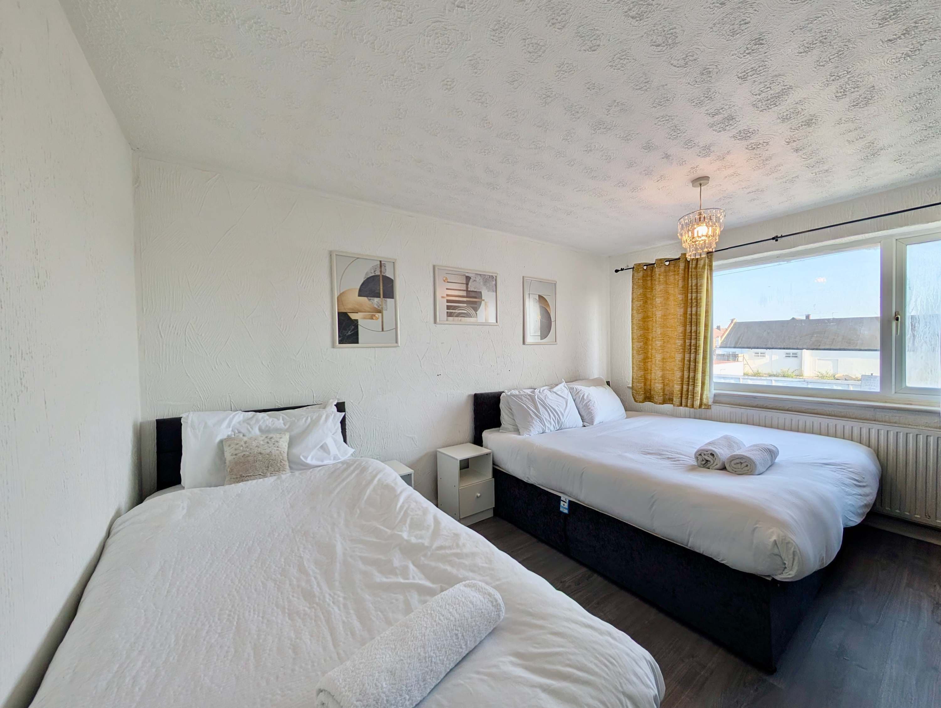 A hotel room with two beds, a nightstand, a lamp, and a window with curtains.