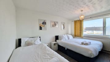 A hotel room with two beds, a nightstand, a lamp, and a window with curtains.