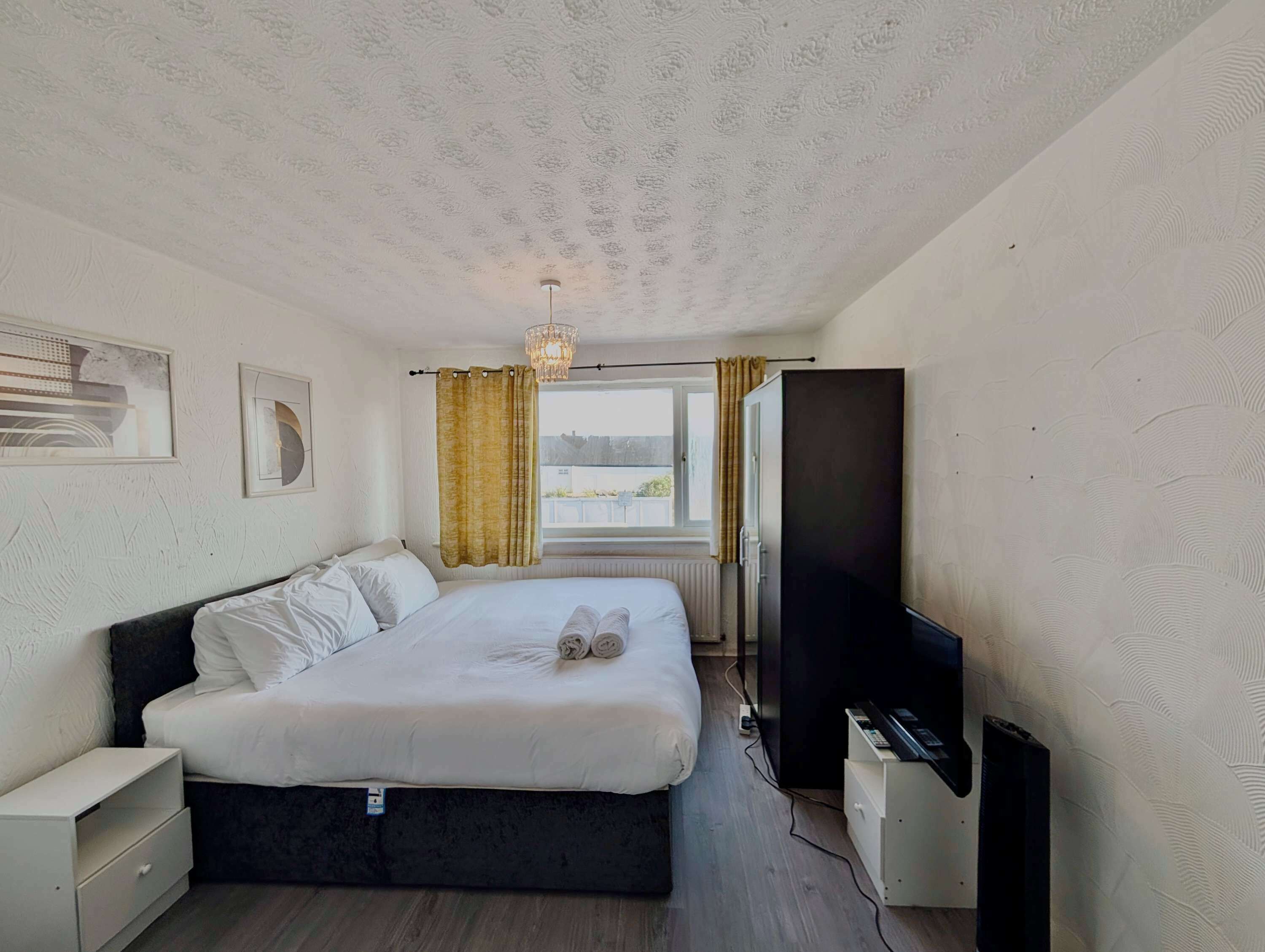 A hotel room with a bed, a television, a window with curtains, and artwork on the wall.