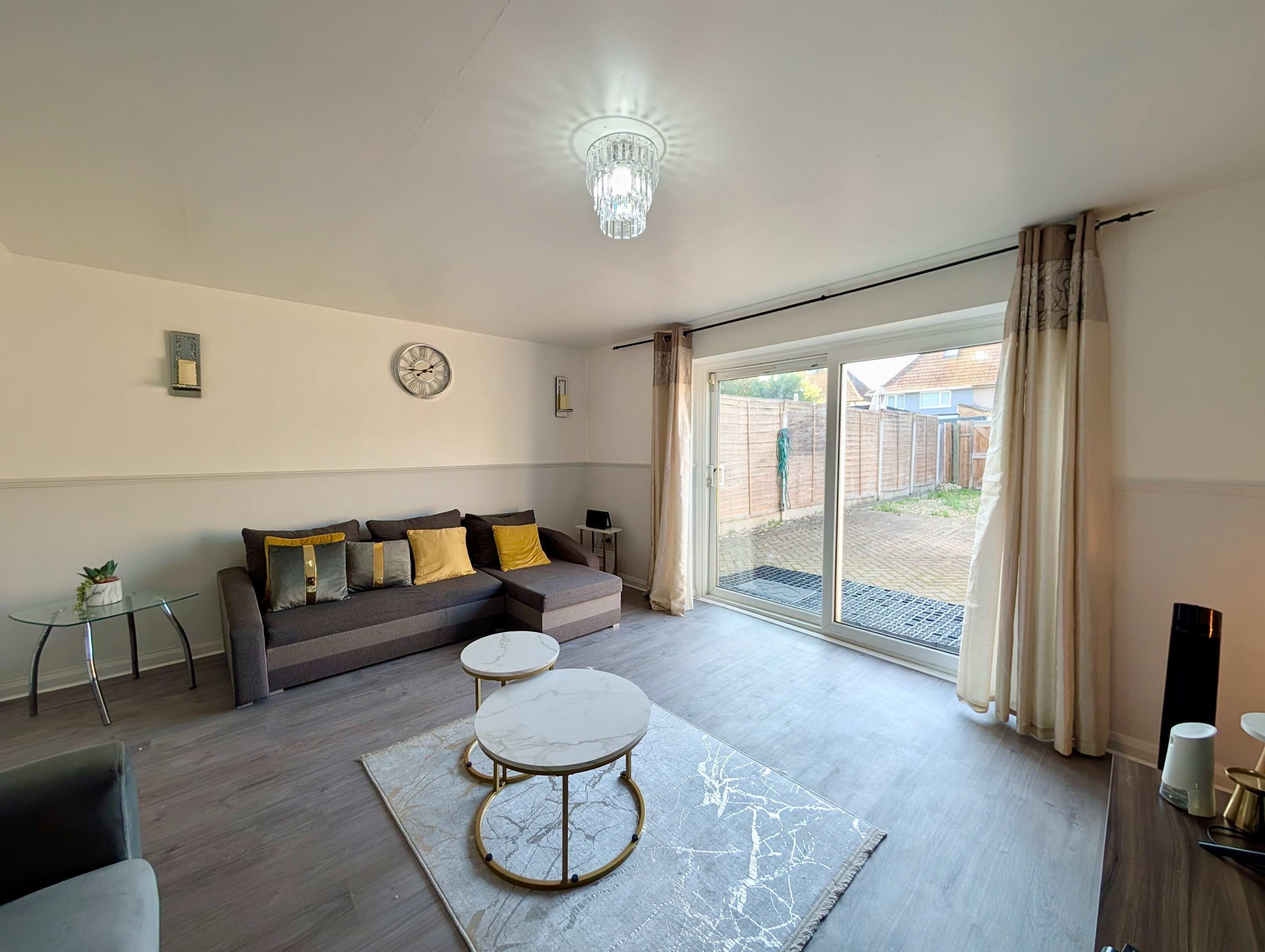 A modern living room with a sofa, two round tables, a chandelier, and a sliding glass door to the outside.