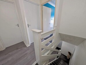 Uma escadaria com corrimão branco e uma porta que dá para um quarto com parede azul.