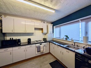 Eine moderne Küche mit weißen Schränken, einer schwarzen Arbeitsplatte, einem eingebauten Ofen und einem Fenster mit Ausblick.