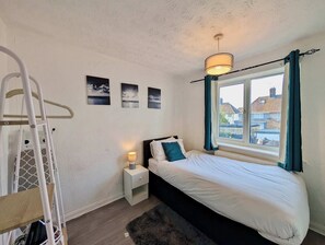 Um quarto com cama, mesa de cabeceira, abajur, escada e janela com cortinas.