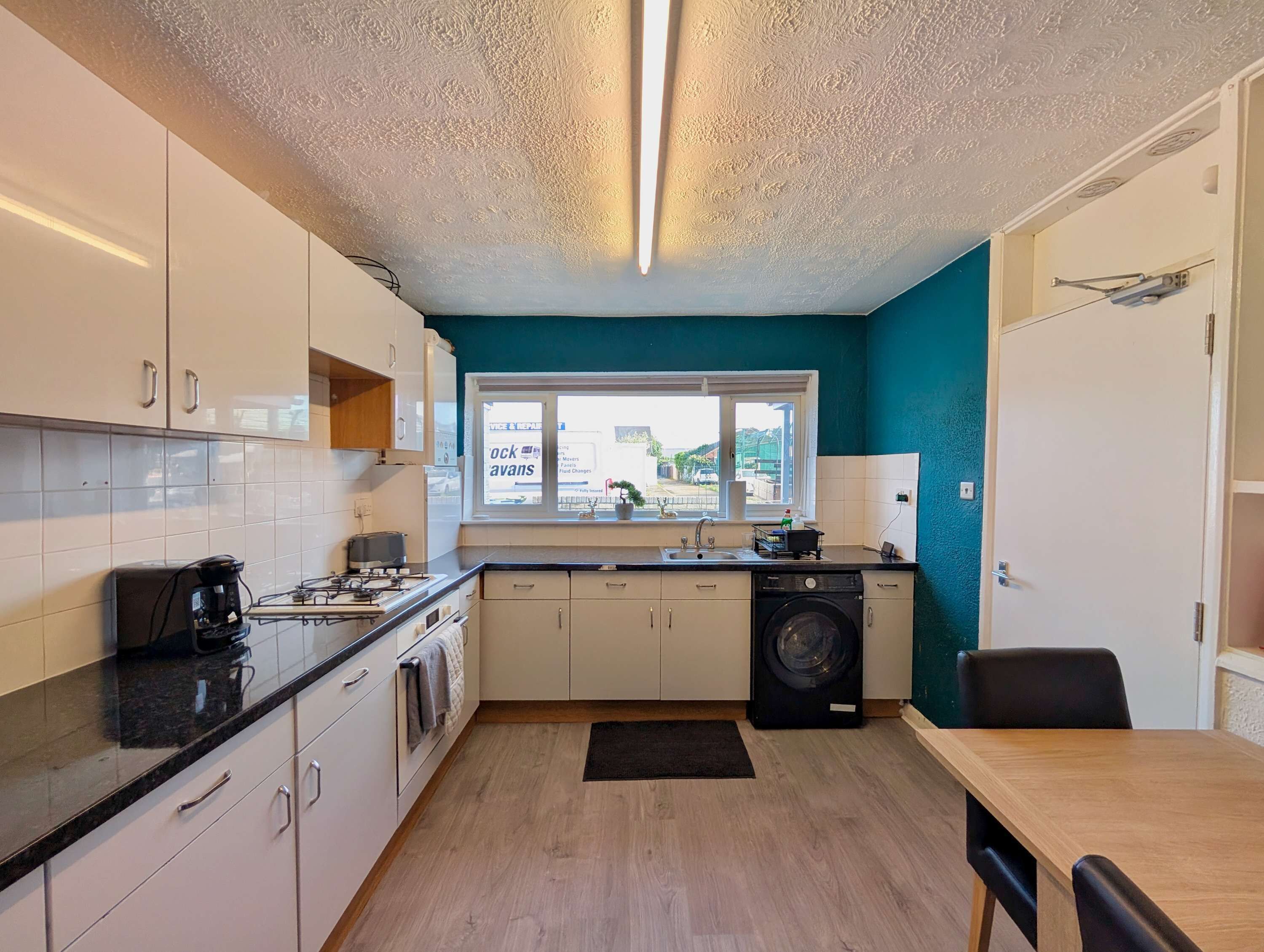 A compact kitchen with white cabinets, a black countertop, a window with a view, and a washing machine.