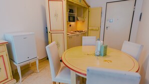 Une cuisine compacte équipée d’un four à micro-ondes, d’une cuisinière et de placards. On y trouve également une table à manger avec des chaises et un réfrigérateur.