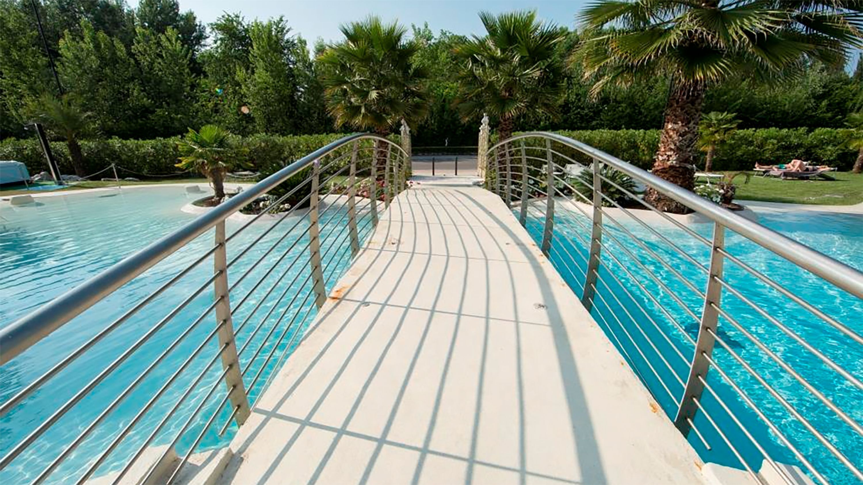 A pool with a bridge leading to a palm tree-lined area.