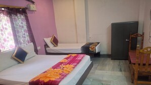 A hotel room with two beds, a wooden chair, a small table, and a refrigerator. - Vishnu Padam Homestay (Tirupati)