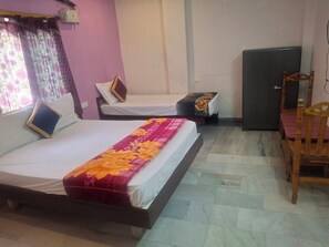 A hotel room with two beds, a wooden chair, a small table, and a refrigerator. - Vishnu Padam Homestay (Tirupati)