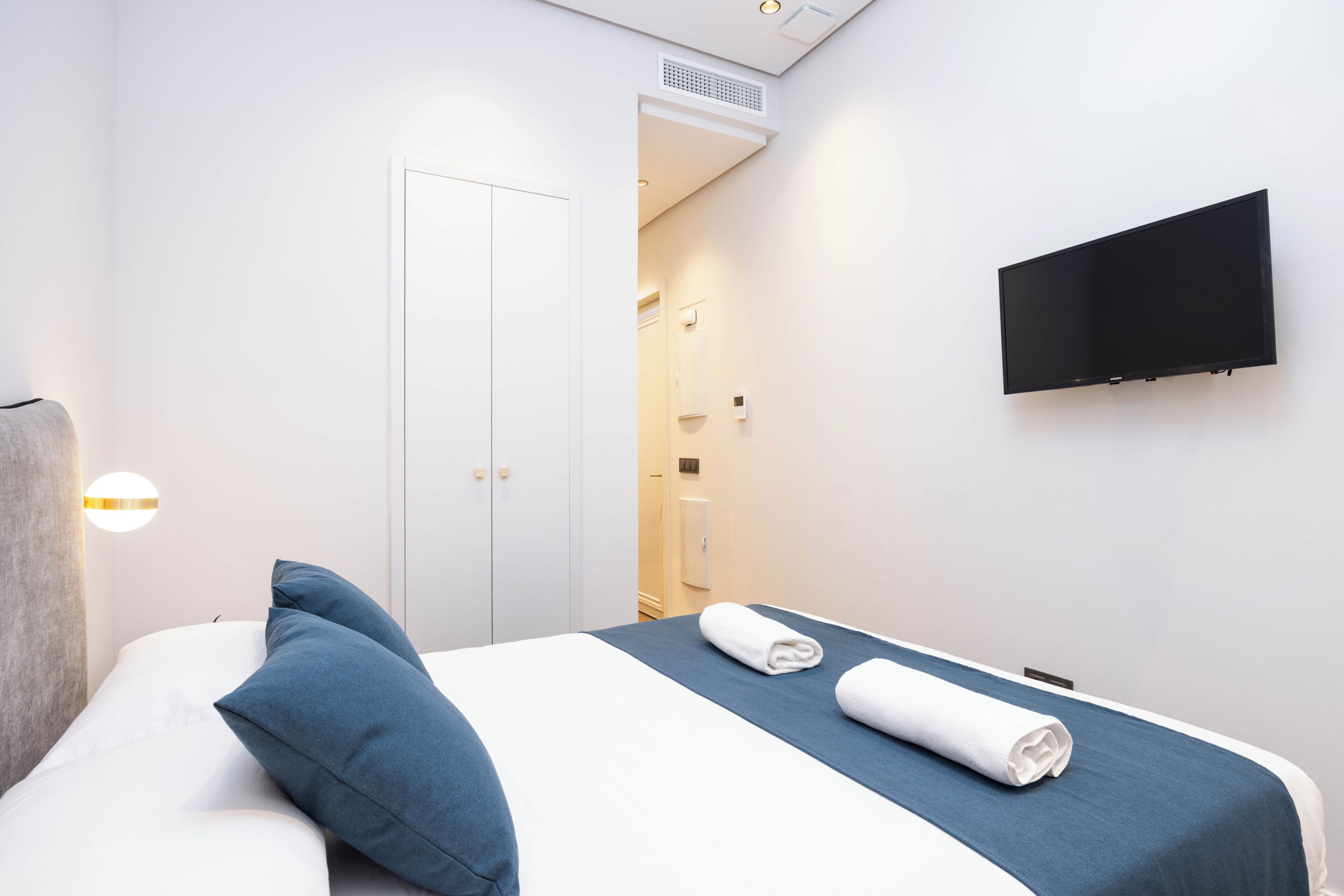 Habitación de hotel con cama, almohadas, televisor y baño visible a través de una puerta abierta.