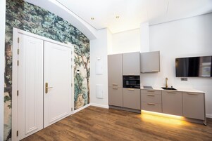 A modern kitchen with white cabinetry, a built-in oven, and a flat-screen TV mounted above the counter.