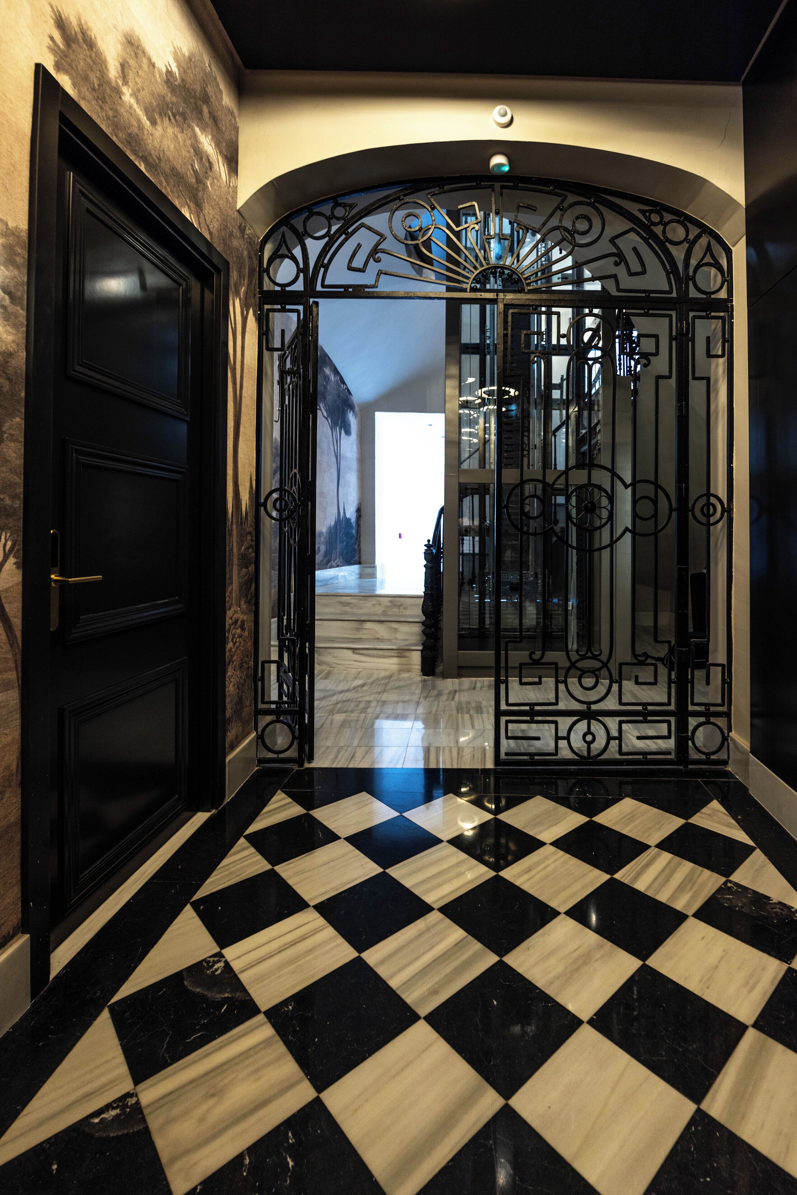 A hallway with a black and white checkered floor, a black door, and an ornate metal gate.