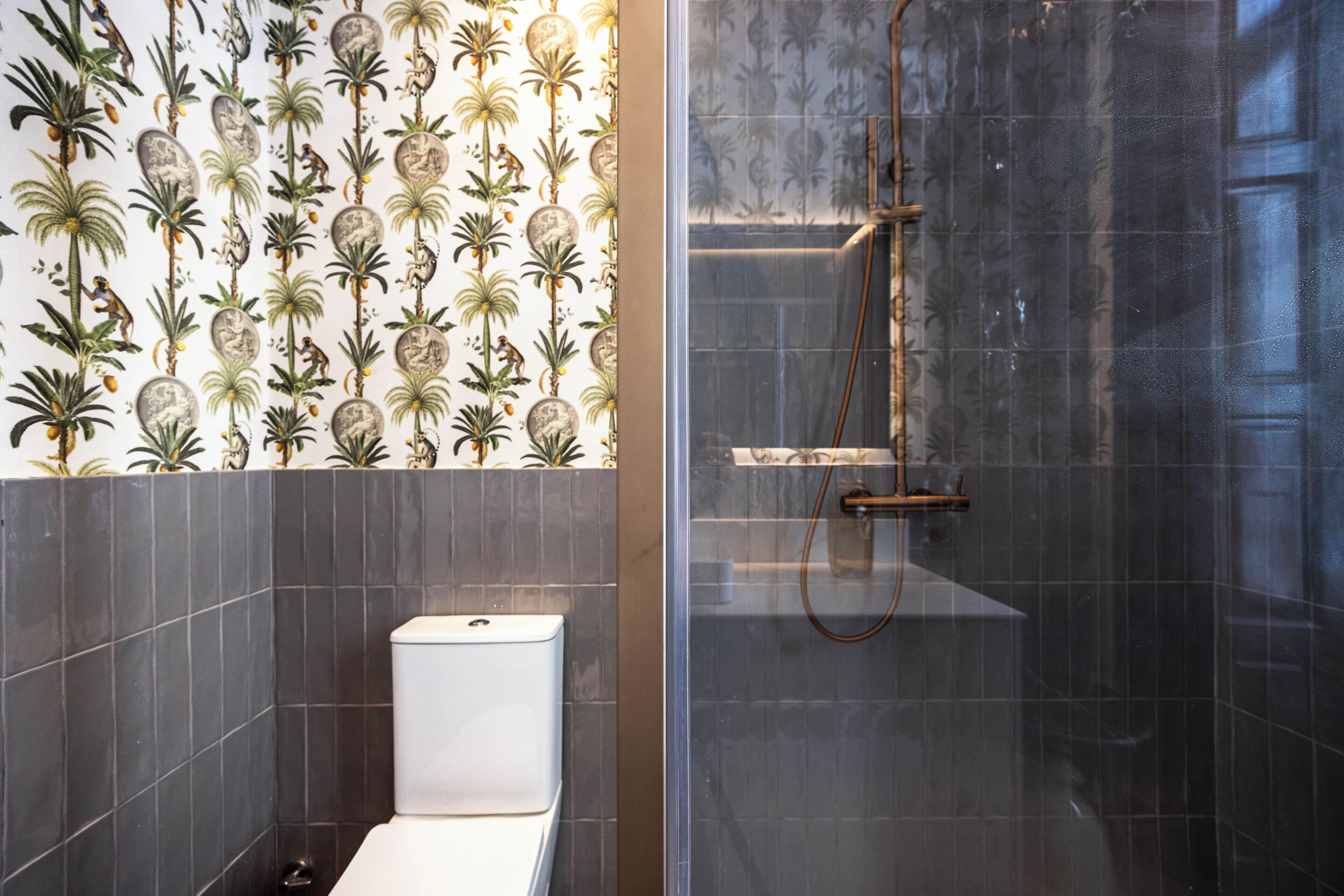 Ein Badezimmer mit Toilette, Dusche und einer Wand mit tropischem Wanddesign.