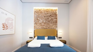 A hotel room with a brick wall accent, a bed with blue and white bedding, and two bedside tables.