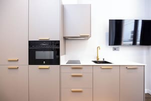 A modern kitchen with a built-in oven, a wall-mounted TV, and a sink with a gold faucet.