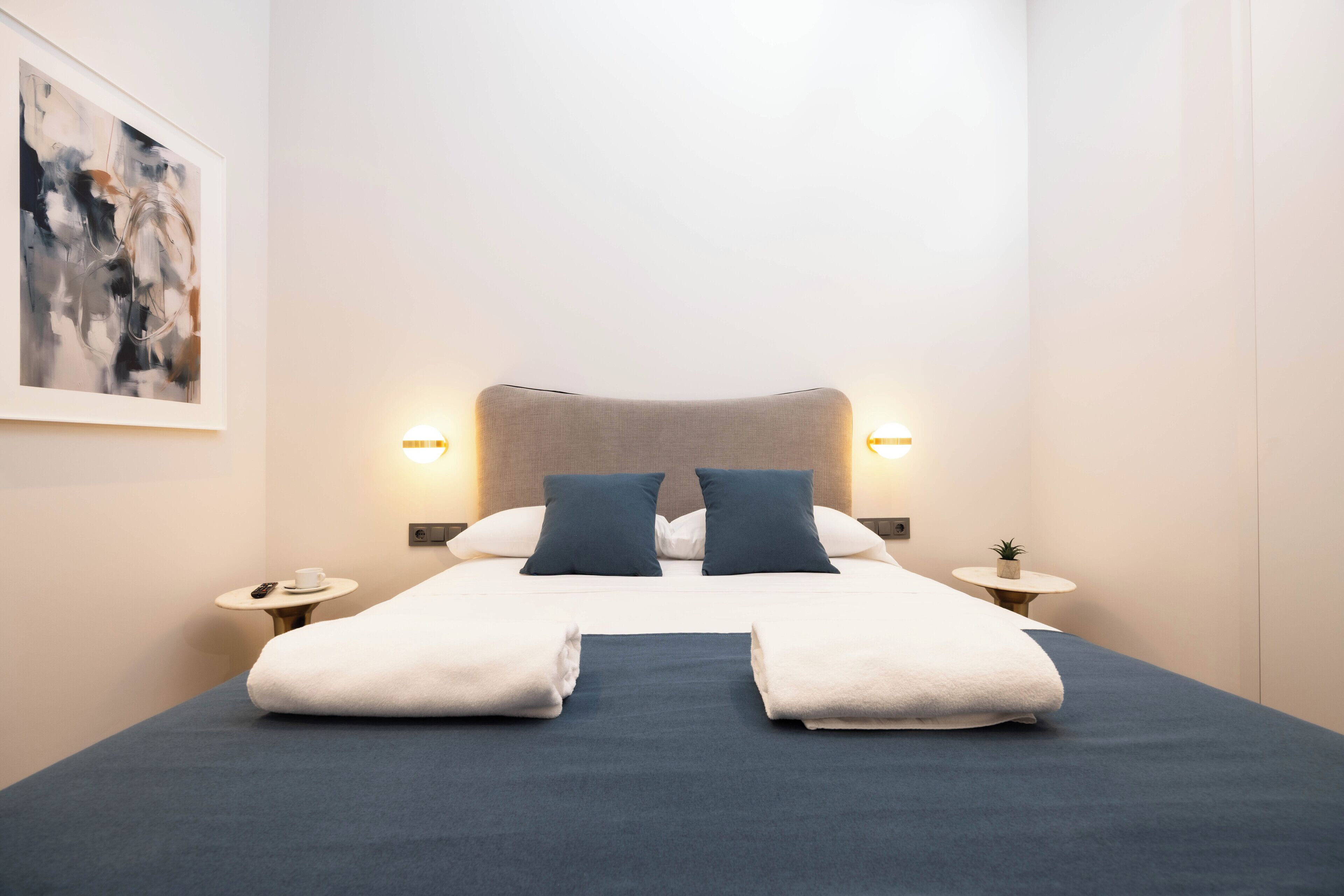 Una camera d'albergo con un letto, due comodini, una lampada a parete e un quadro.