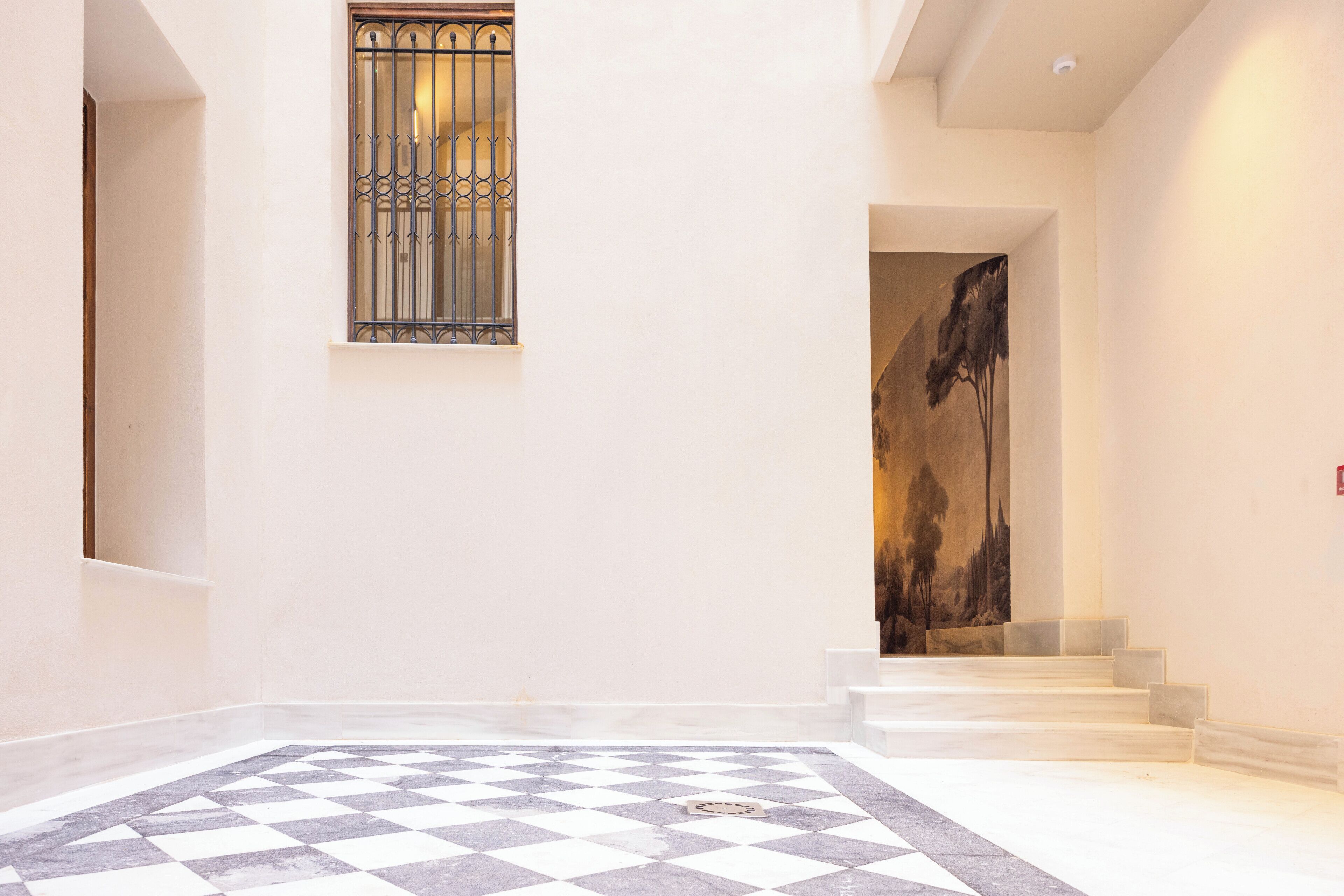 A hotel lobby with a checkered floor, a staircase, and a painting on the wall.