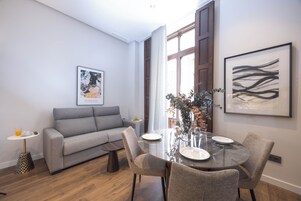 Una sala de estar moderna con un sofá gris, una mesa de comedor preparada para dos personas y obras de arte en las paredes.