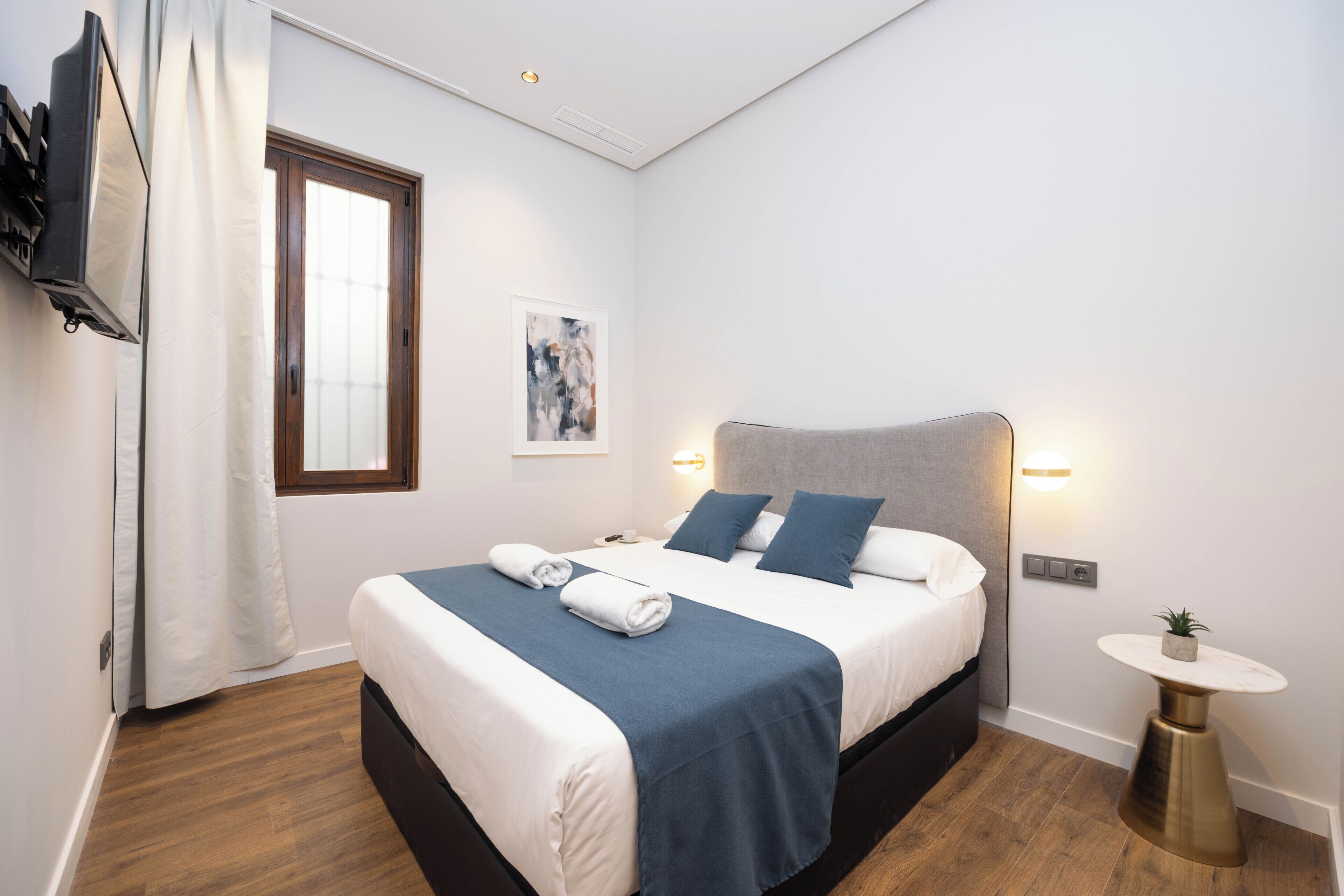 Ein modernes Hotelzimmer mit Bett, Nachttisch und einer kleinen Topfpflanze.