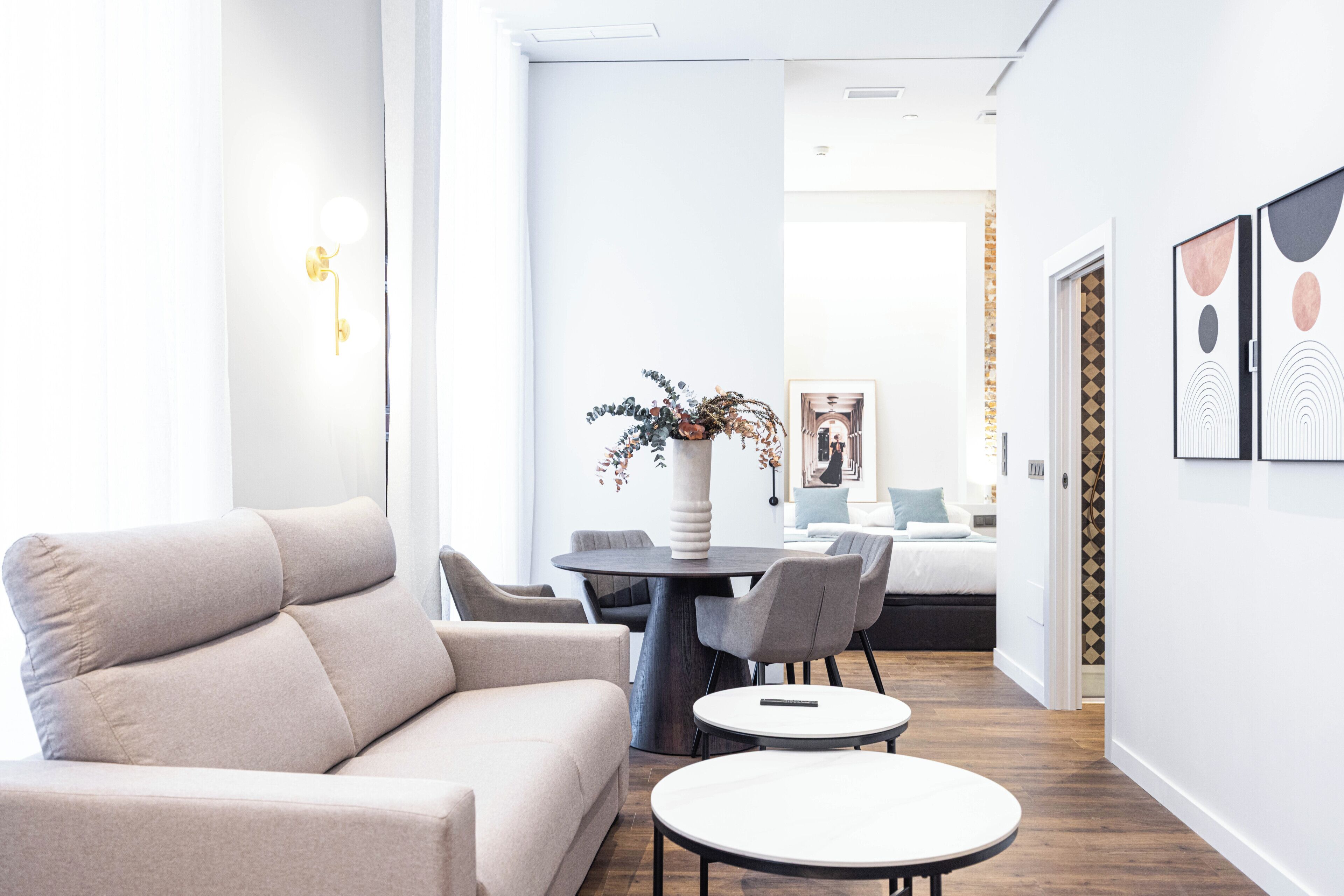 Una habitación de hotel moderna con sofá, dos mesas redondas, una planta en maceta y obras de arte en las paredes.