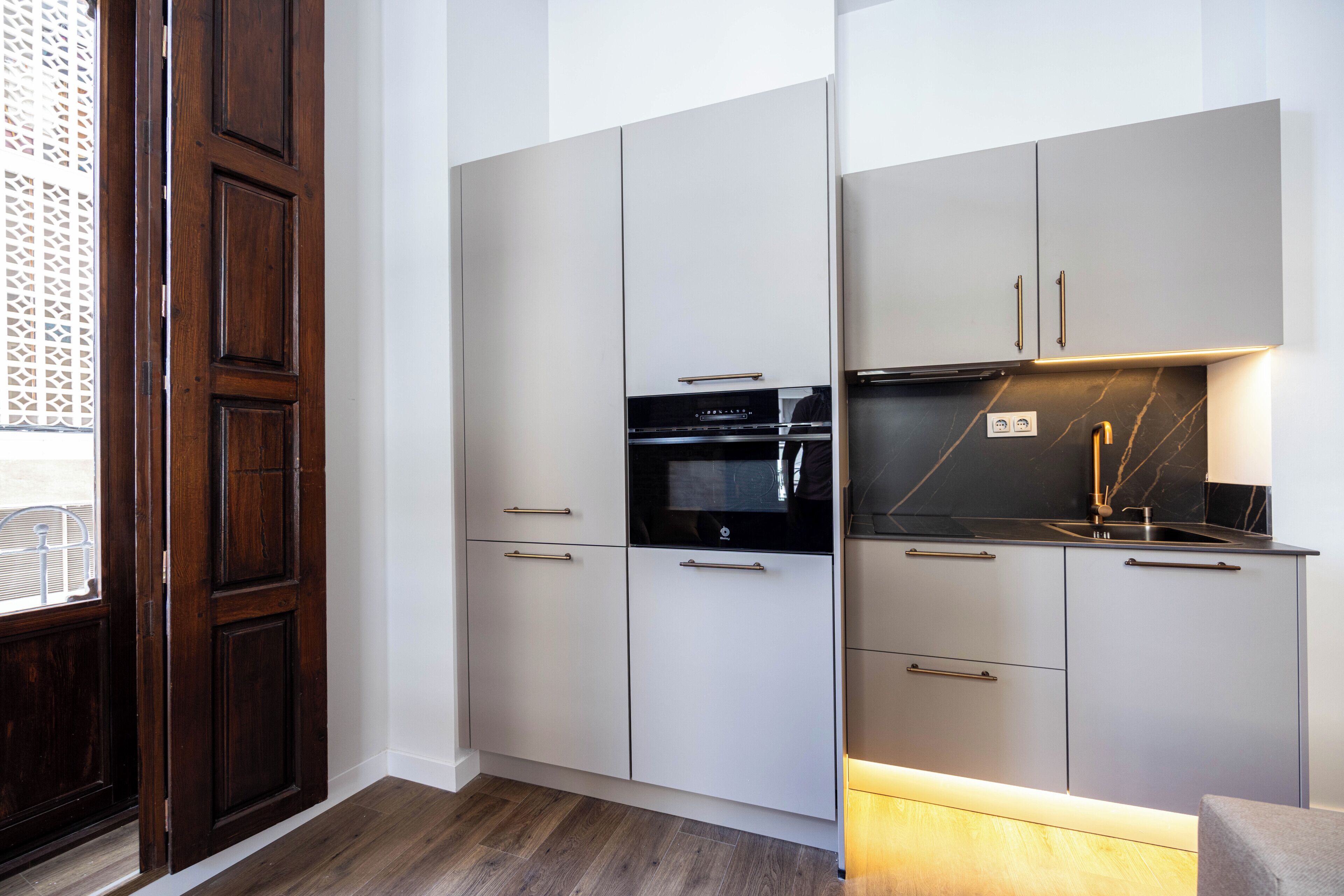A compact kitchen with built-in appliances, a sink, and a window with a decorative screen.