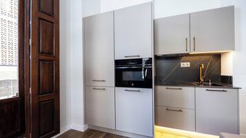 A compact kitchen with built-in appliances, a sink, and a window with a decorative screen.