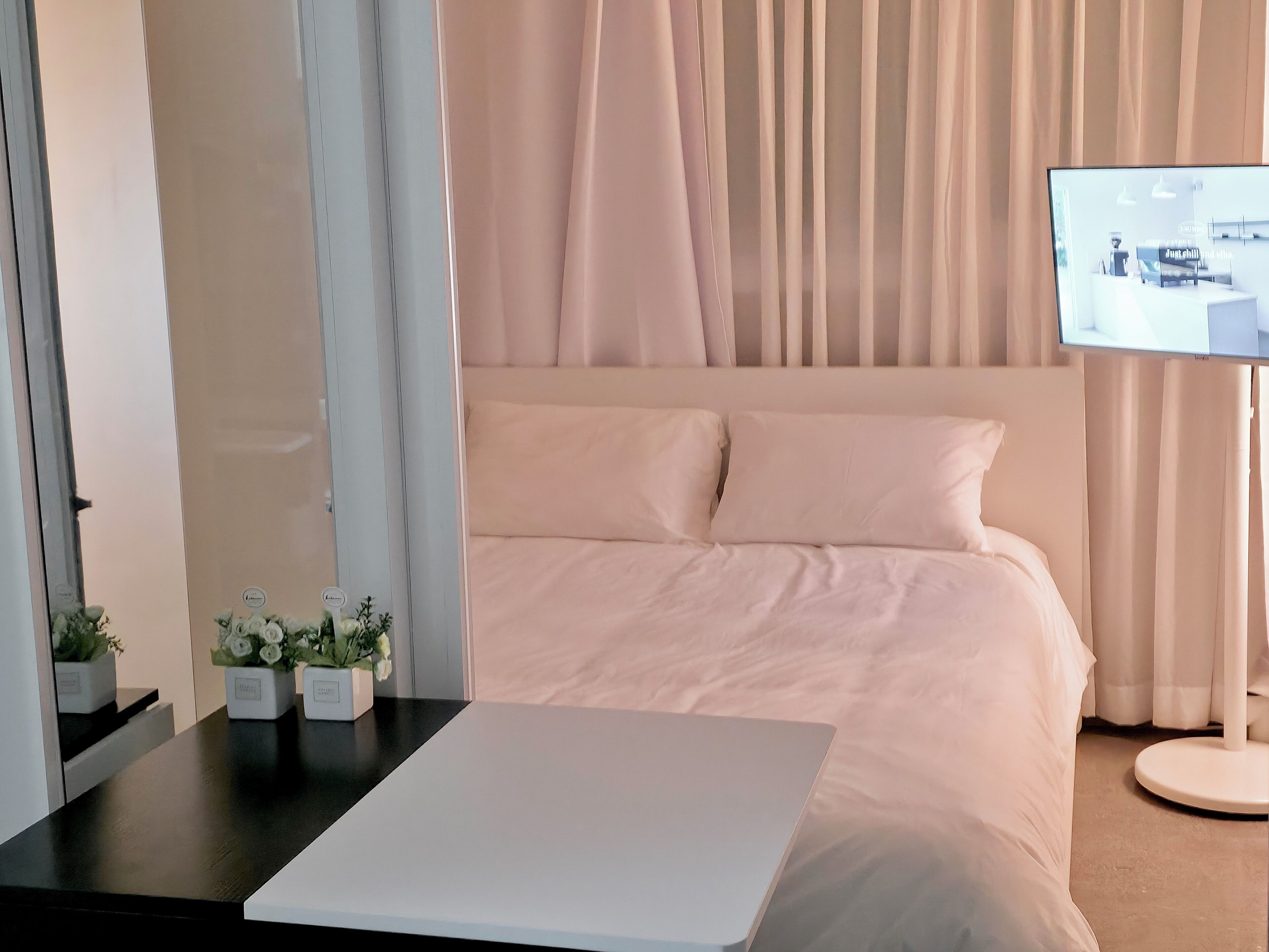 Une chambre d’hôtel moderne dotée d’un grand lit, d’un téléviseur à écran plat fixé au mur et d’une petite table agrémentée d’objets décoratifs.