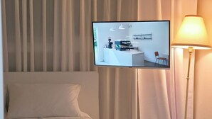Une chambre d’hôtel avec un lit, un téléviseur fixé au mur, une lampe et des rideaux.