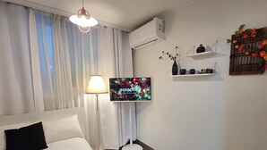 A hotel room with a bed, a TV, a lamp, a small round table, and a decorative wall piece. - House Gangnam - offers a modern, cozy space (Seoul)