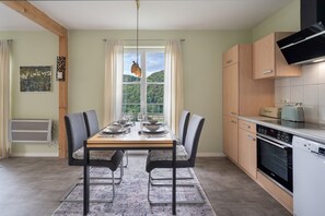 A modern kitchen with a dining area, featuring a large window, wooden cabinets, and a built-in oven. - Wiesentflair Holiday Home with Panoramic Views in Muggendorf – 2 Bedrooms, 4 Guests (Wiesenttal)