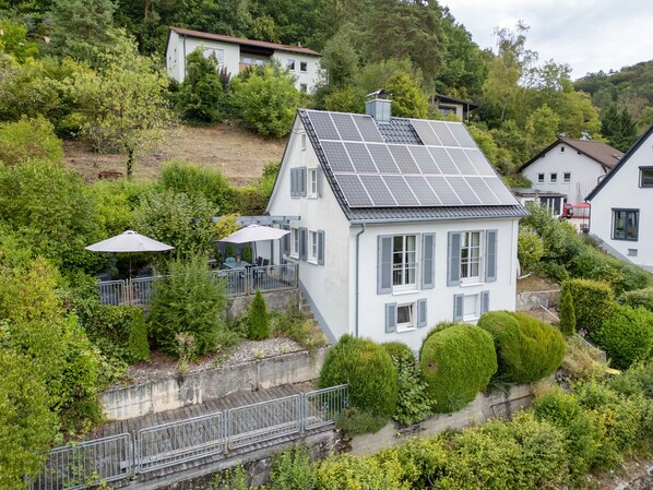 Una casa con techo solar, rodeada de exuberante vegetación y un pequeño patio.