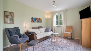 Een woonkamer met een bank, fauteuils, een bijzettafeltje, een schilderij en een televisie.