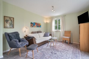 A living room with a sofa, armchairs, a small table, a painting, and a television.