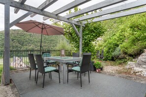 Un patio techado con una mesa y sillas, rodeado de vegetación y vistas a un área boscosa.