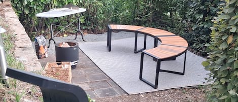 An outdoor patio with a curved wooden bench, a round table, and a black grill.