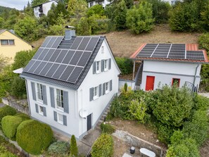 Zona residencial con dos casas, una con paneles solares y una puerta roja, rodeada de vegetación.