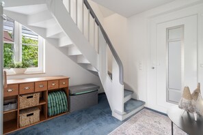 A staircase leading to a landing with a white door, a wooden bench with storage baskets, and a window with greenery outside.
