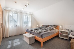 Un dormitorio con una cama de madera, una mesita de noche con lámpara, un pequeño estante y una ventana con cortinas.