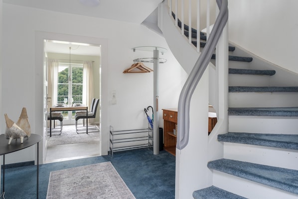 A staircase with a handrail, a dining area with a table and chairs, and a view through a door to a balcony.