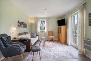 A modern living room with a sofa, armchairs, a small table, and a television.