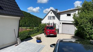 Een woonwijk met een wit huis, een rode auto en een zwarte auto die ervoor geparkeerd staan.