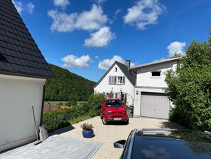 A residential area with a white house, a red car, and a black car parked in front. - Wiesentflair Holiday Home with Panoramic Views in Muggendorf – 2 Bedrooms, 4 Guests (Wiesenttal)
